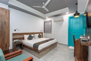 A bedroom with a bed, bedside table, nightstand, and a desk with a chair. - Chhavi Hotels (Noida)