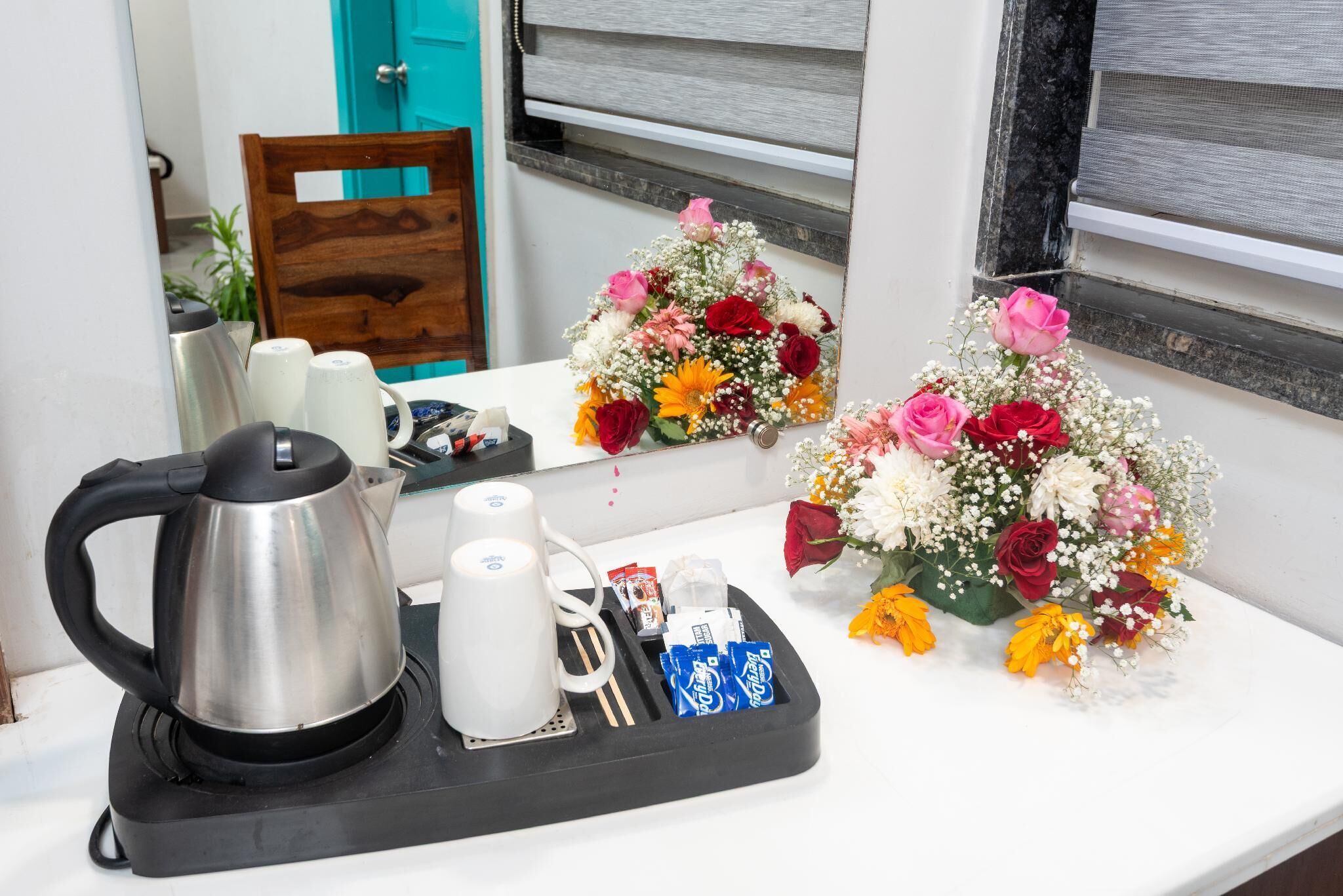 Een ontbijt opstelling met een waterkoker, kopjes en een schaal met koffieportiezakjes op een witte tafel.