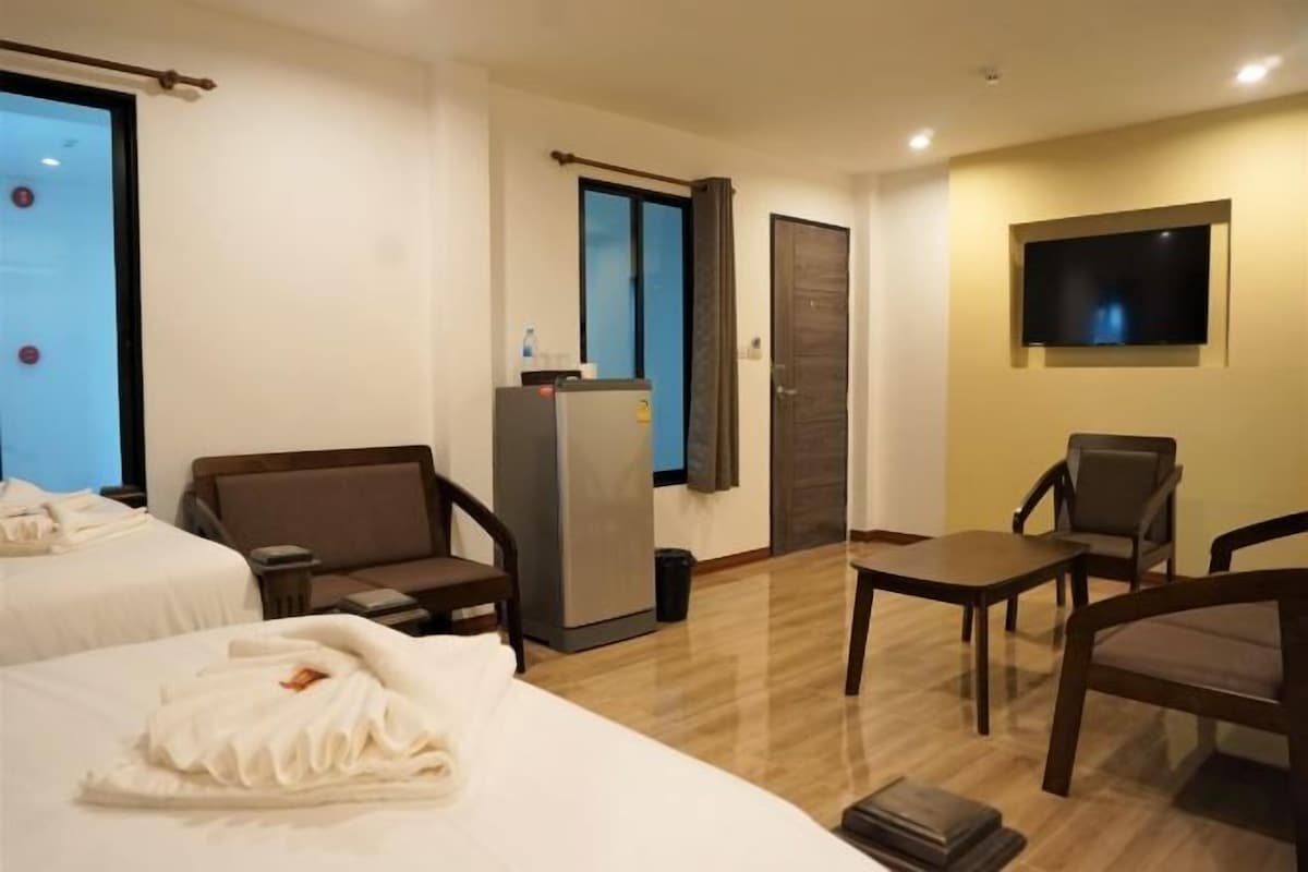 A hotel room with two beds, a desk, a chair, a TV, and a refrigerator.