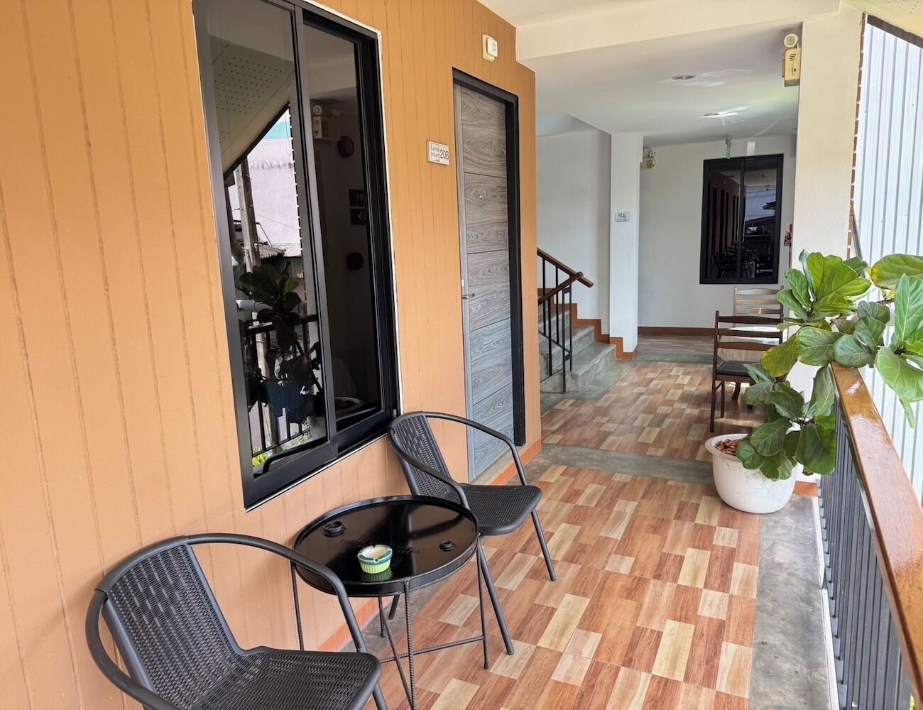Un balcon avec deux chaises et une petite table, un pot de fleurs et une vue sur l’intérieur du bâtiment.