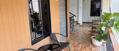 Un balcon avec deux chaises et une petite table, un pot de fleurs et une vue sur l’intérieur du bâtiment.