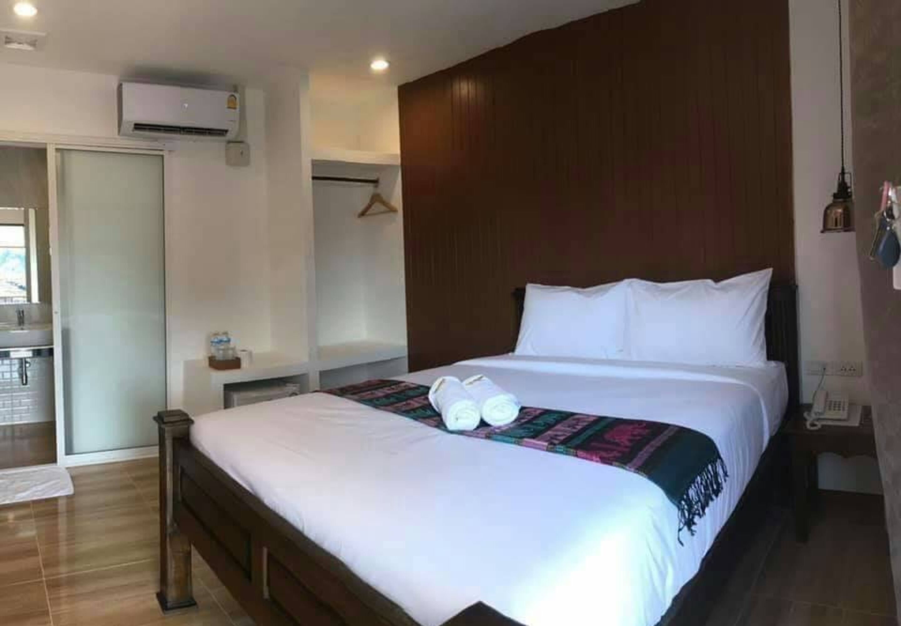 Ein Hotelzimmer mit einem großen Bett, einem Nachttisch, einer Pendelleuchte und einem kleinen Schreibtisch mit Telefon.