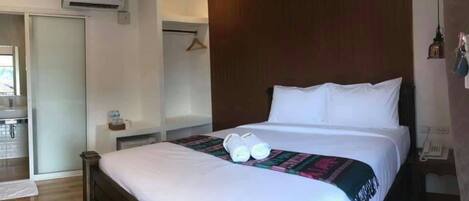 A hotel room with a large bed, a bedside table, a hanging light, and a small desk with a telephone.