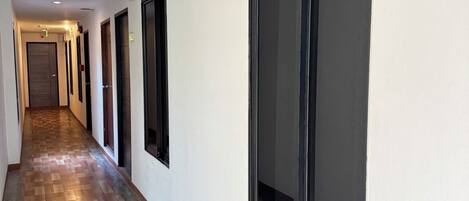 A hallway with a fire exit sign, wooden flooring, and large windows.