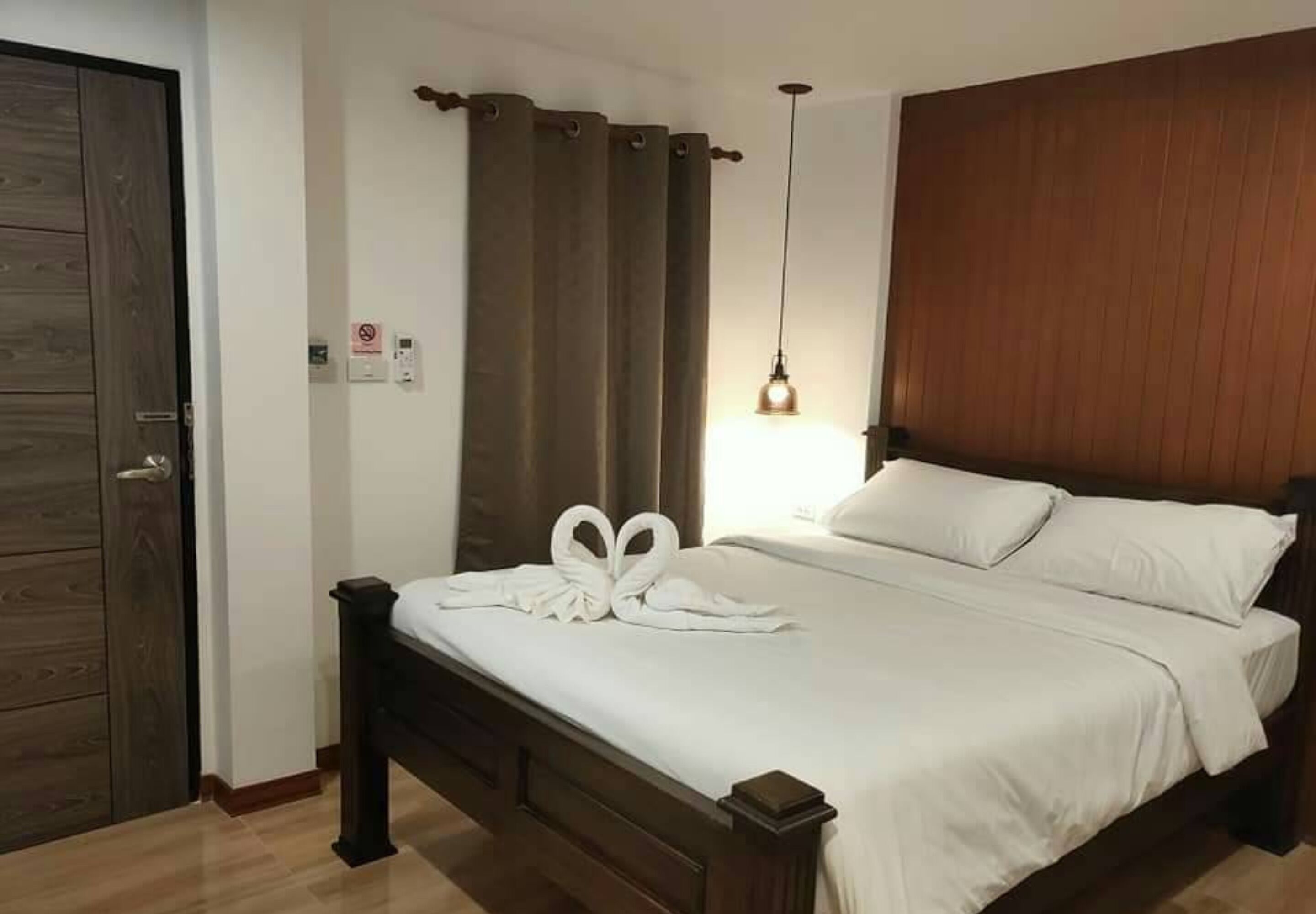 A neatly made bed with white linens and a pair of towels arranged in a heart shape on the headboard.
