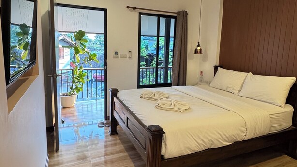 Een slaapkamer met een houten bed, een balkon met een bloempot en uitzicht op groen.