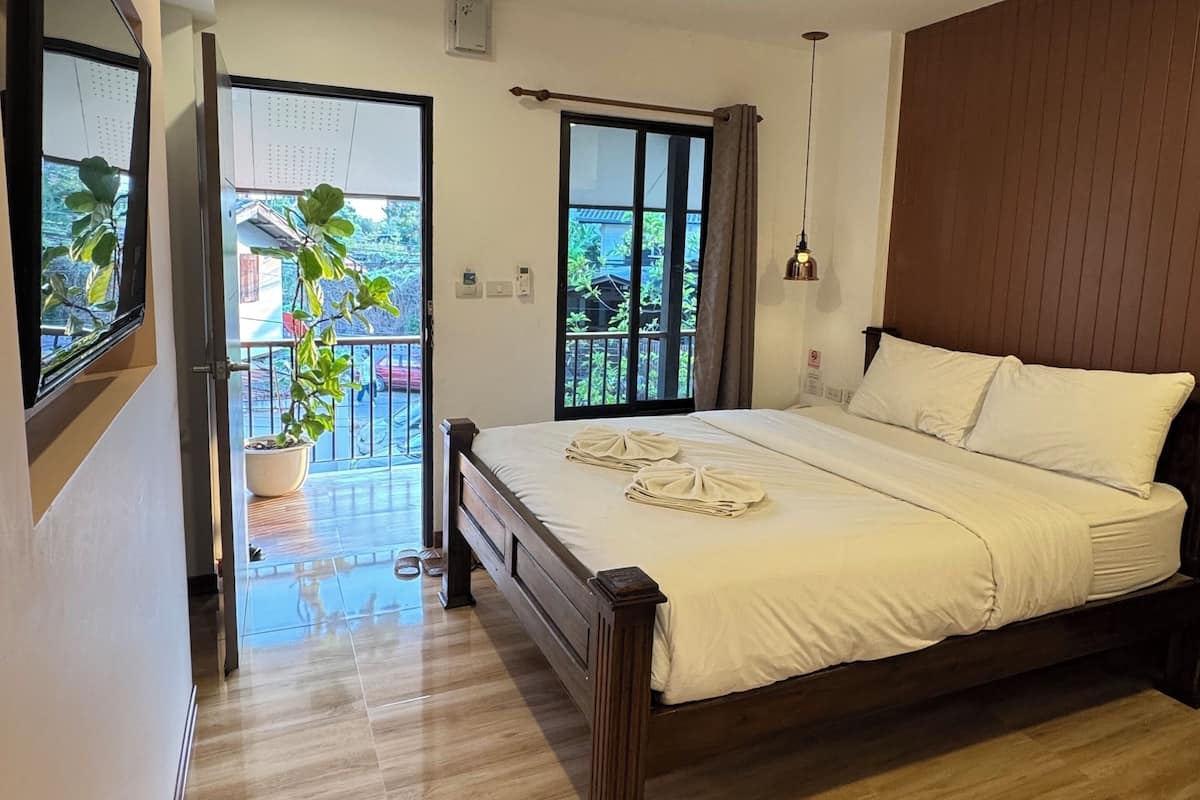 Quarto com cama de madeira, varanda com planta em vaso e vista para o verde lá fora.