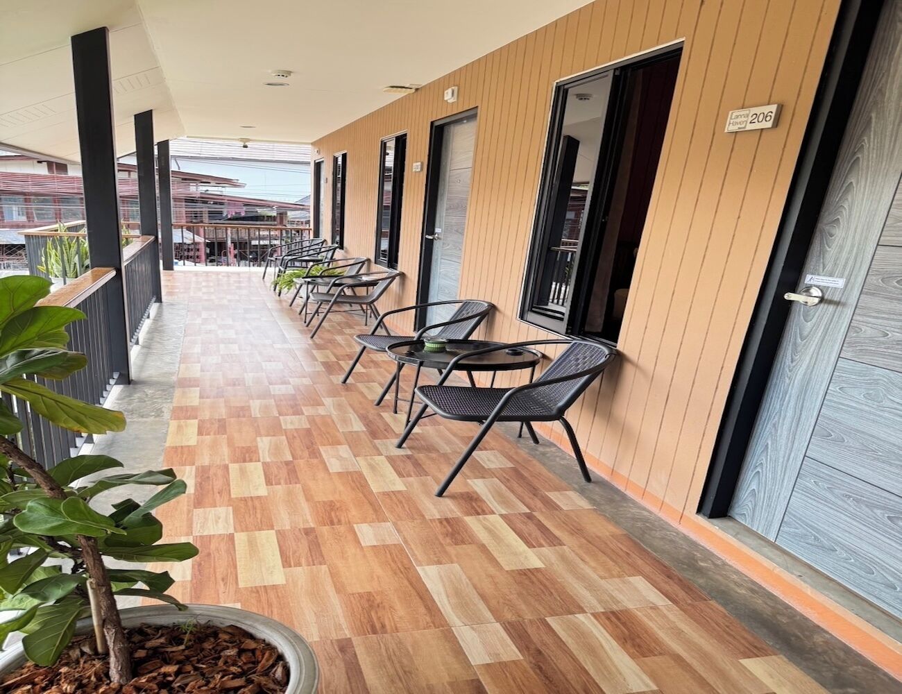 Un pasillo con piso de madera, sillas y mesas de metal negro, que conduce a puertas con un cartel que indica el número de habitación 206.