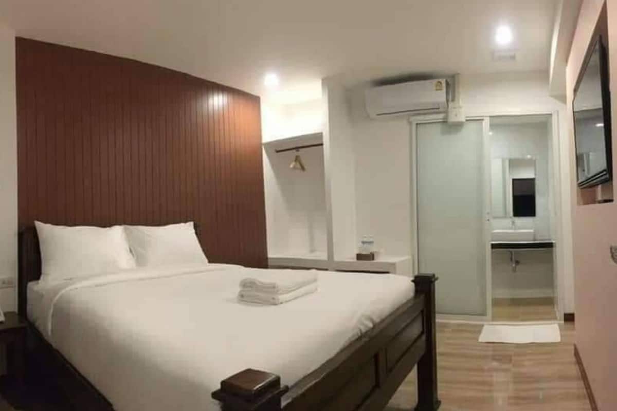 Quarto de hotel com uma cama grande, cabeceira de madeira, mesa de cabeceira, guarda-roupa e banheiro com espelho, além de um aparelho de ar condicionado.