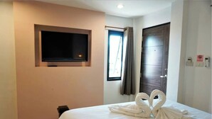 Een hotelkamer met een bed, een flatscreen televisie aan de muur, een raam met gordijnen en een deur.
