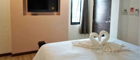 A hotel room with a bed, a flat-screen TV mounted on the wall, a window with curtains, and a door.