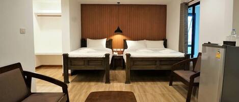 A hotel room with two beds, a sofa, a small table, a refrigerator, and a wooden accent wall.