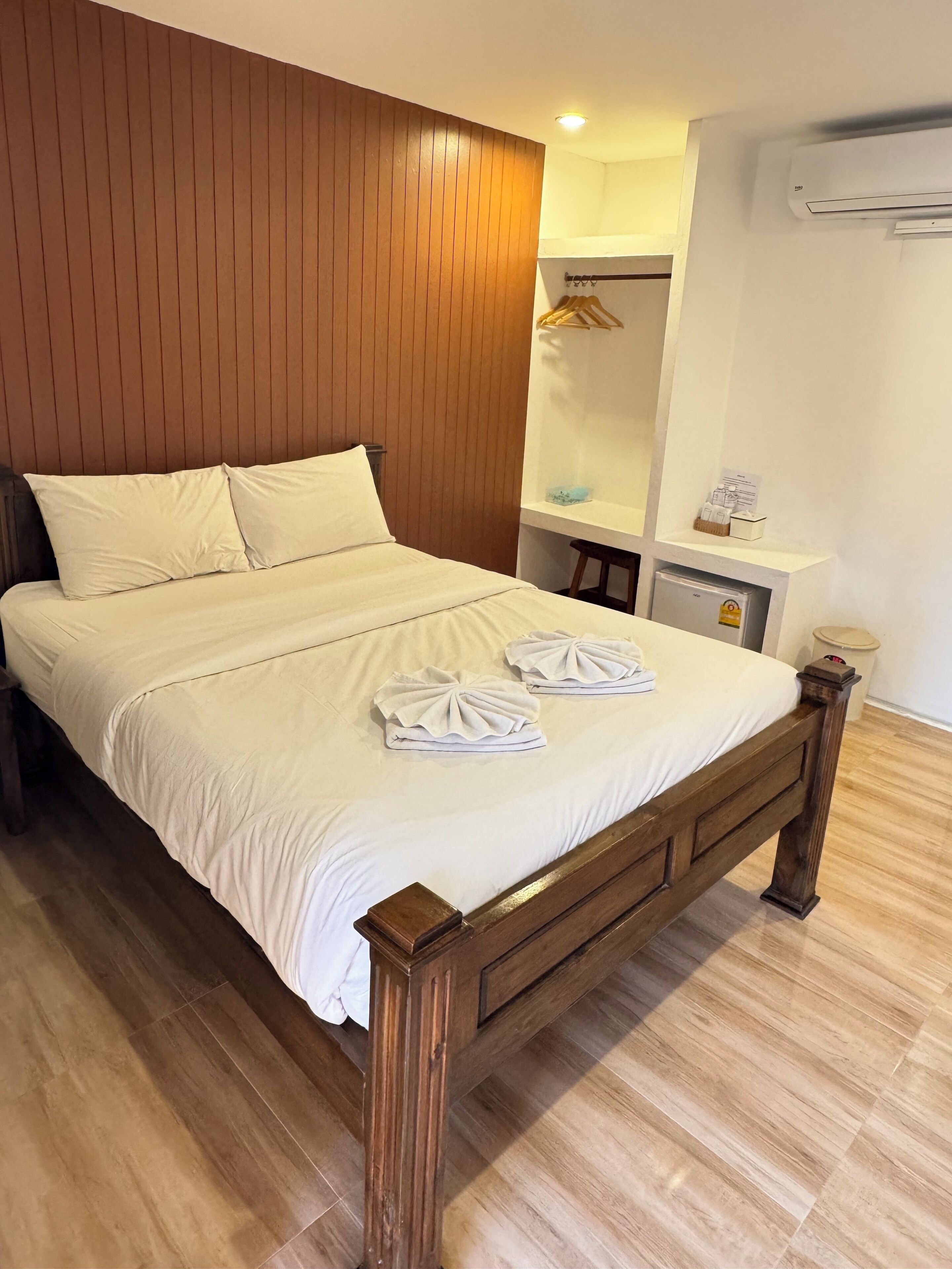 Ein ordentlich bezogenes Bett mit weißen Leinen und Handtüchern, ein Holz-Kopfteil und ein Holzboden.