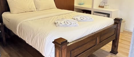 Ein ordentlich bezogenes Bett mit Holz Kopfteil, ein kleiner Nachttisch mit Lampe und eine Wand-Klimaanlage.