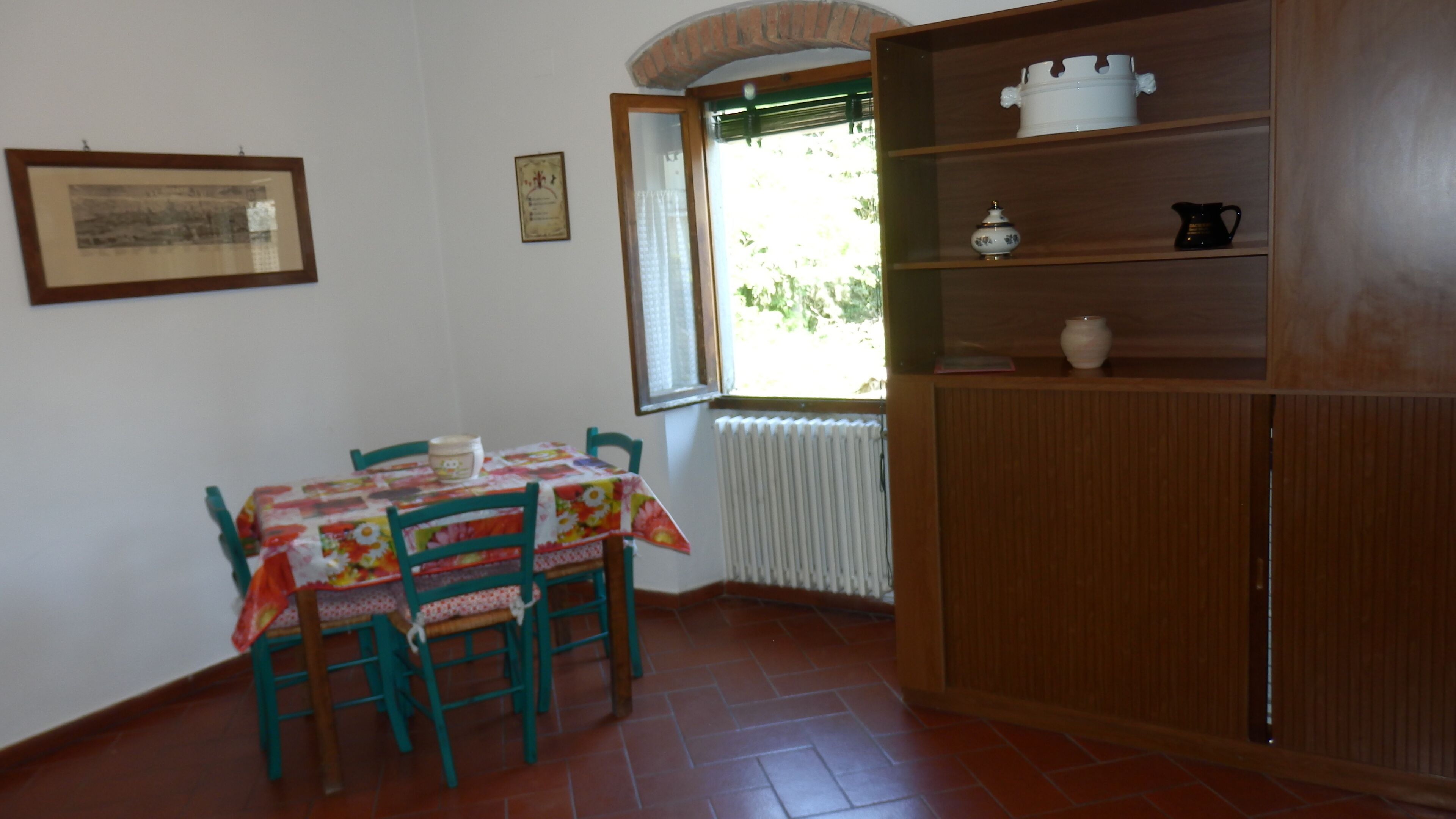 Un comedor con una mesa dispuesta para dos personas, un radiador y un aparador de madera con utensilios de cocina.