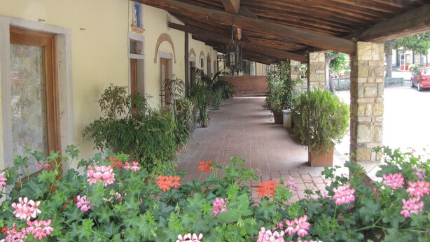A covered walkway with potted plants and flowers, leading to a building with arched doorways and a brick wall. - Residence Casprini da Omero (Greve in Chianti)