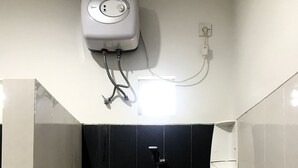 Un bagno con parete doccia in piastrelle nere, un termosifone bianco a parete e uno scaffale bianco.