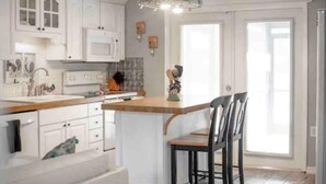 Een keuken met witte kasten, een houten eiland met stoelen en een groot raam.