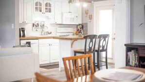 Een moderne keuken met witte kastjes, een eethoek met twee stoelen en een kroonluchter.