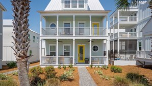 Una casa frente al mar de dos pisos con un porche delantero, varios balcones y una puerta amarilla.