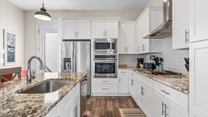Una cocina moderna con armarios blancos, electrodomésticos de acero inoxidable, encimeras de granito y suelo de madera.