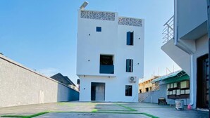 Um edifício moderno com telhado plano, uma pequena varanda e um pátio pavimentado com grama sintética.
