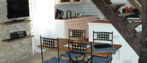 A cozy kitchen with a dining table, chairs, a TV, and a staircase.