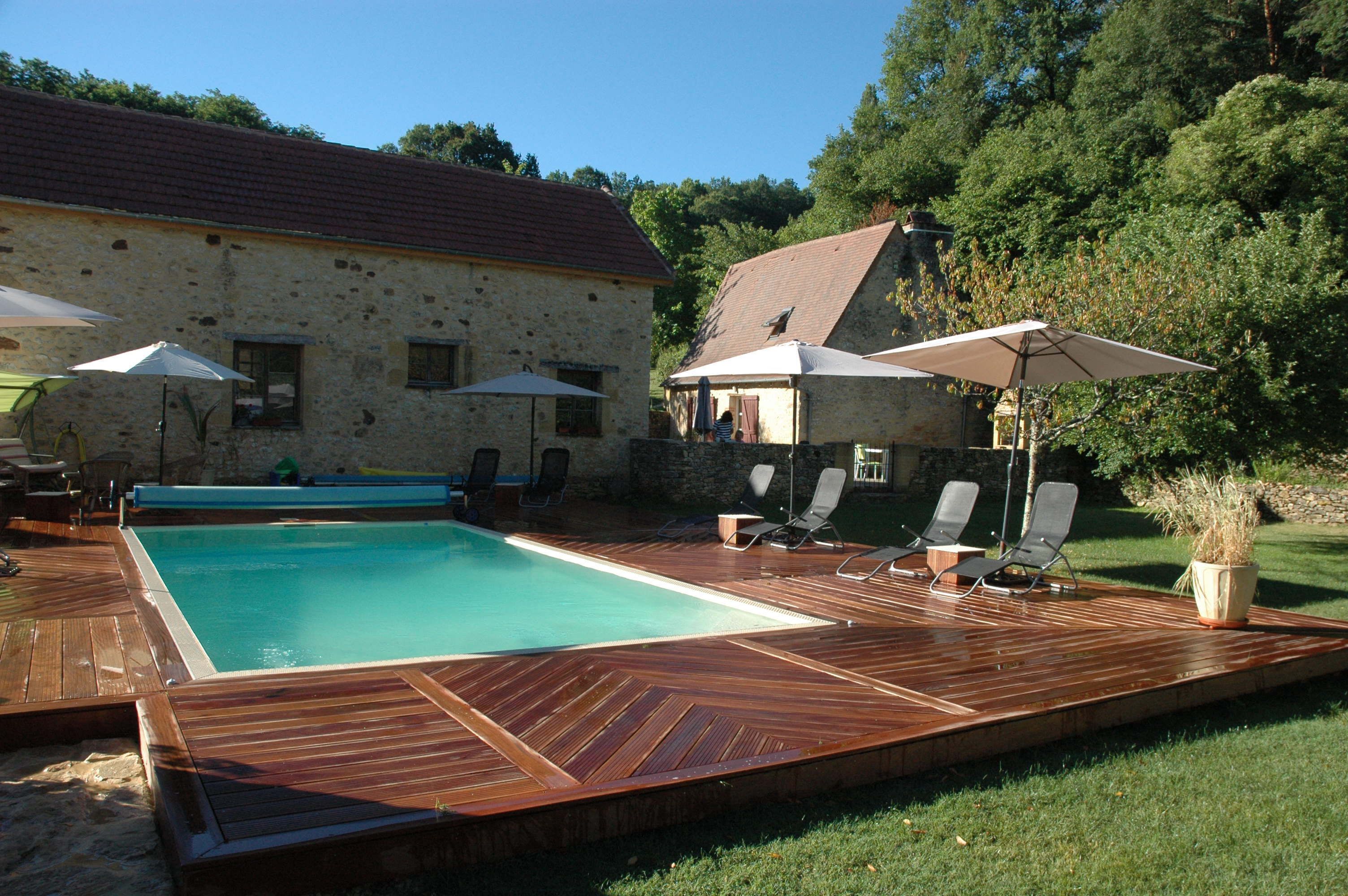 A swimming pool with a wooden deck, lounge chairs, and umbrellas.