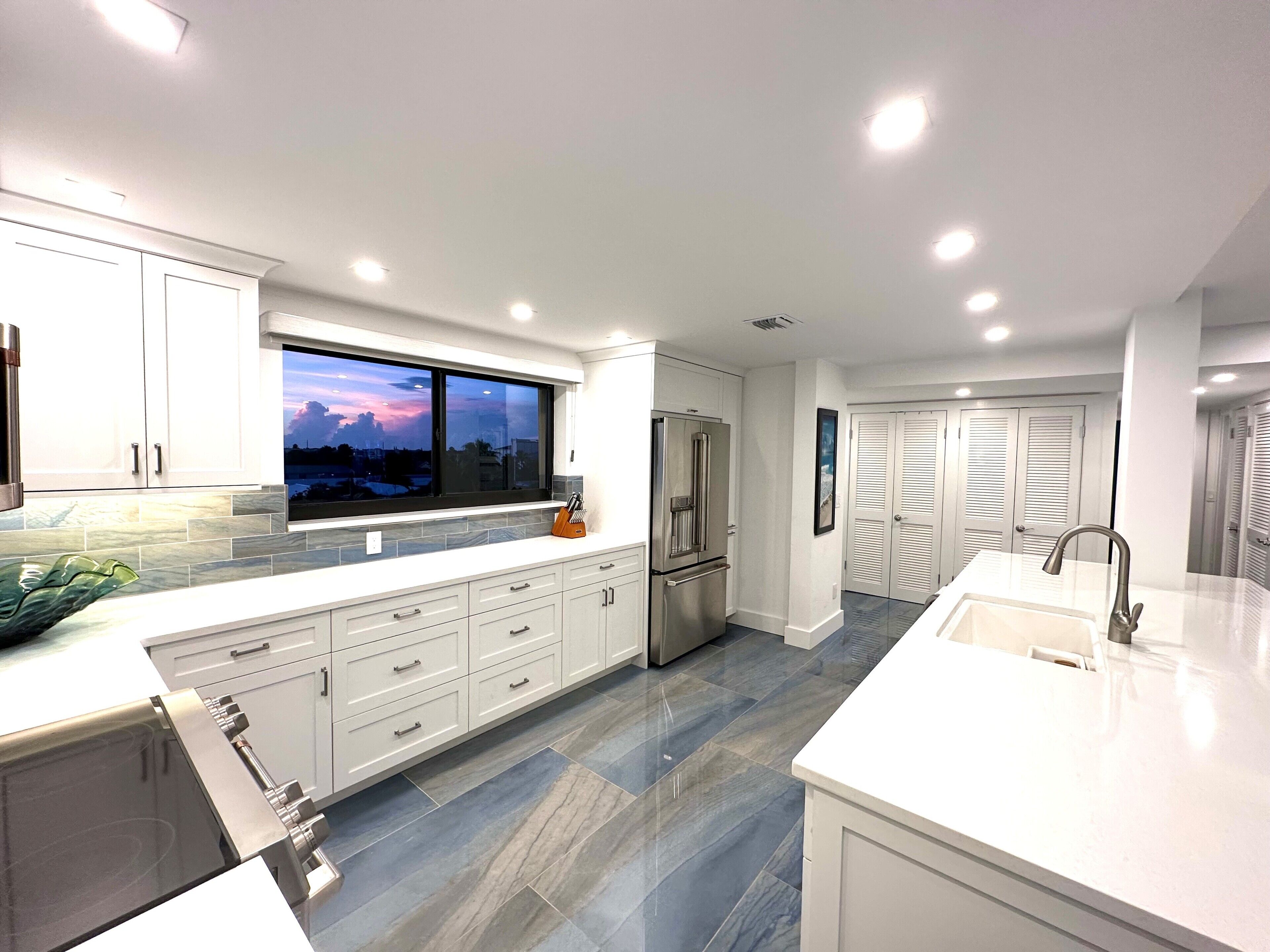 A modern kitchen with white cabinets, a large window, and a built-in refrigerator.