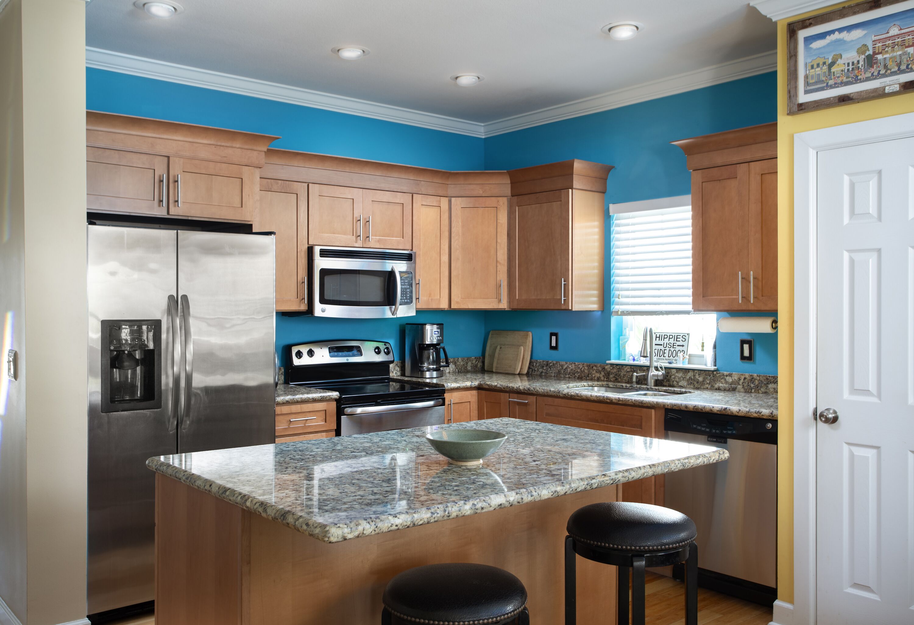Una cocina moderna con armarios de madera, electrodomésticos de acero inoxidable, encimeras de granito y una isla central con taburetes.