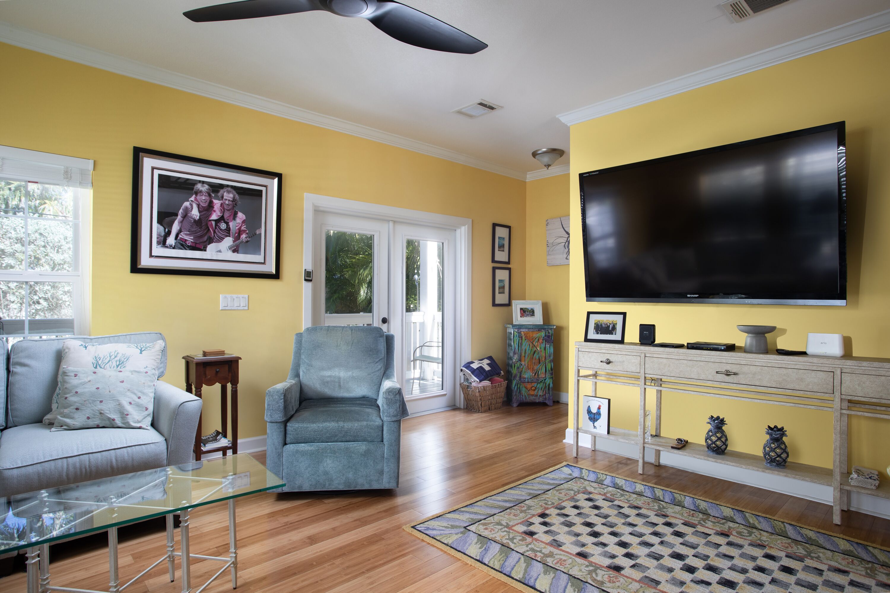 Un salón con sofá, sillón, una mesa de centro de vidrio y televisor sobre un mueble.