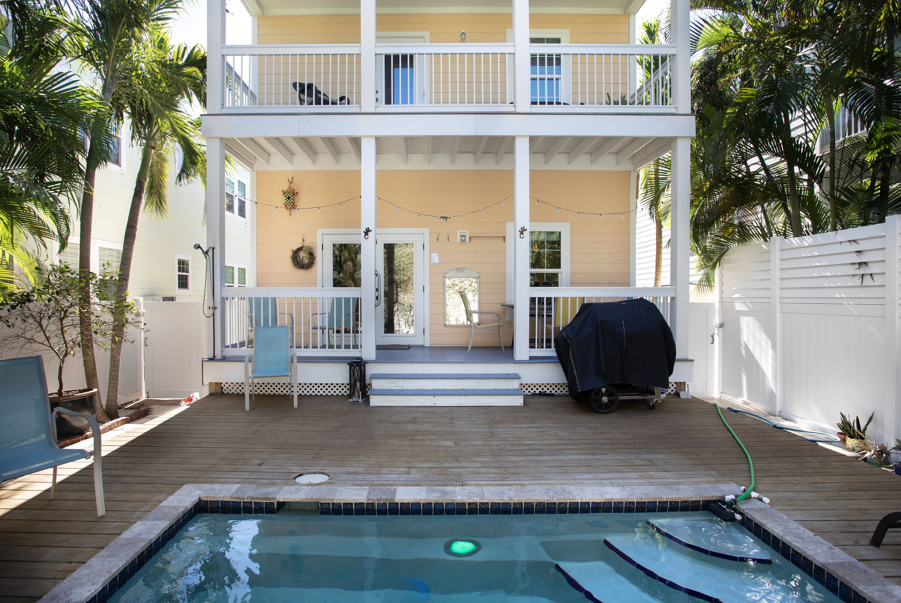 A two-story house with a wooden deck, a swimming pool, and a covered grill area.