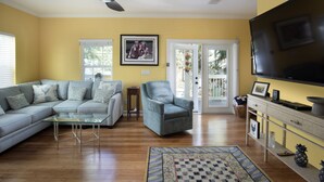 A living room with a sectional sofa, a glass coffee table, a grey armchair, a TV, and a fireplace. - Sunshine Escape- 3 bedroom 3 bath w/ parking for 2, private pool, balcony (Key West)