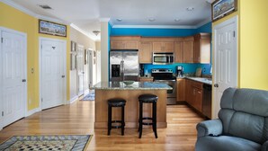 A modern kitchen with wooden cabinets, stainless steel appliances, and a central island with stools. - Sunshine Escape- 3 bedroom 3 bath w/ parking for 2, private pool, balcony (Key West)