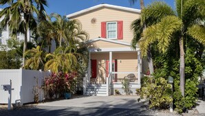 A two-story house with a porch, surrounded by palm trees and other tropical plants. - Sunshine Escape- 3 bedroom 3 bath w/ parking for 2, private pool, balcony (Key West)