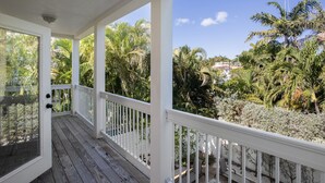 A covered porch with white railings and a view of tropical vegetation. - Sunshine Escape- 3 bedroom 3 bath w/ parking for 2, private pool, balcony (Key West)