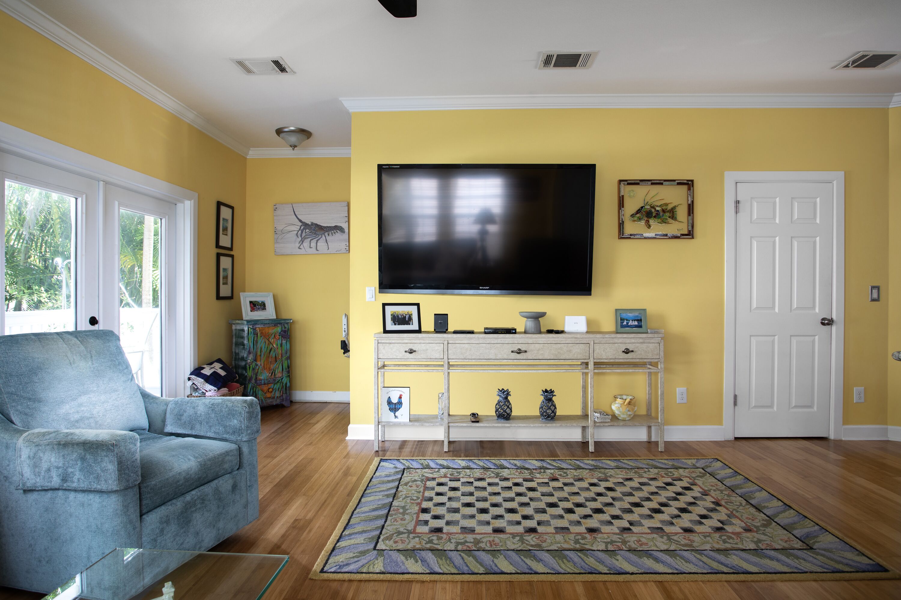 Un salón con un televisor de pantalla plana grande, un sillón azul, un tapete estampado y una puerta blanca.