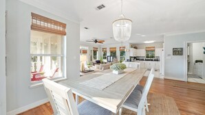 A spacious living area with a large wooden dining table, white chairs, and a chandelier.
