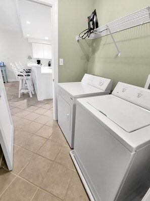 A laundry area with two white washers and dryers, a drying rack, and a small kitchenette with a bar stool.