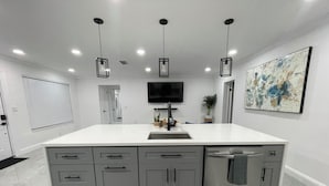 A modern kitchen with a large island, grey cabinets, a built-in dishwasher, and pendant lighting. - Pool House 3/2: Grill, Mural and Ping Pong Table (Sunrise)
