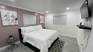 A bedroom with a bed, a TV mounted on the wall, and artwork on the walls. - Pool House 3/2: Grill, Mural and Ping Pong Table (Sunrise)