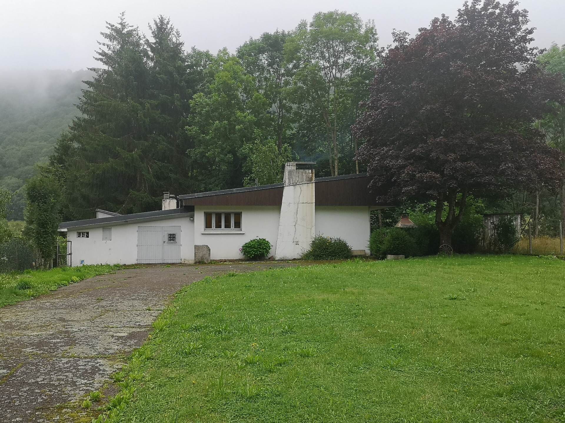Ein weißes Haus mit Schornstein, umgeben von einem grünen Rasen und Bäumen.