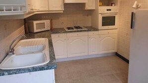 Een keuken met witte kastjes, een spoelbak, een magnetron, een oven en een gasfornuis.