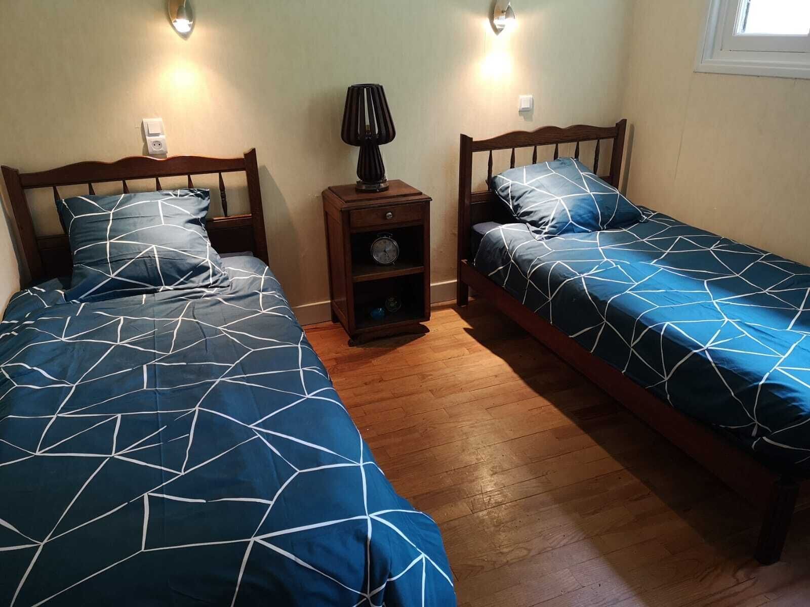 Un dormitorio con dos camas individuales, cabeceros de madera, una mesita de noche con lámpara y un aplique de pared.