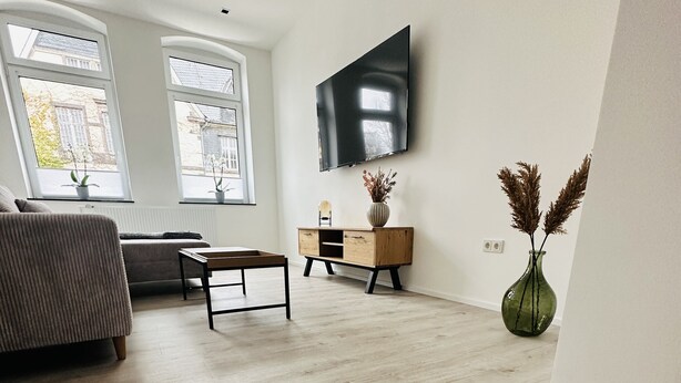 A modern living room with a sofa, coffee table, and a TV mounted on the wall. - Vacation apartment in Obernkirchen (Obernkirchen)