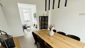 A modern dining area with a wooden table, six chairs, and a vase of flowers. There is a black cabinet and a wooden cabinet with a black metal frame. - Vacation apartment in Obernkirchen (Obernkirchen)