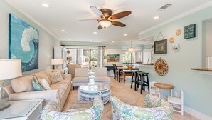 A spacious living room with a ceiling fan, a dining area, and a kitchen in the background. - Golf Cart ~ Multiple Pools ~ Screened Back Patio (Miramar Beach)