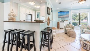 A kitchen with white cabinets, a stainless steel refrigerator, and a bar area with black stools. - Golf Cart ~ Multiple Pools ~ Screened Back Patio (Miramar Beach)