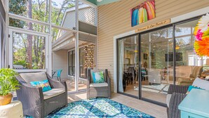 A covered patio with wicker furniture, a patterned rug, and a view of the interior through glass doors. - Golf Cart ~ Multiple Pools ~ Screened Back Patio (Miramar Beach)