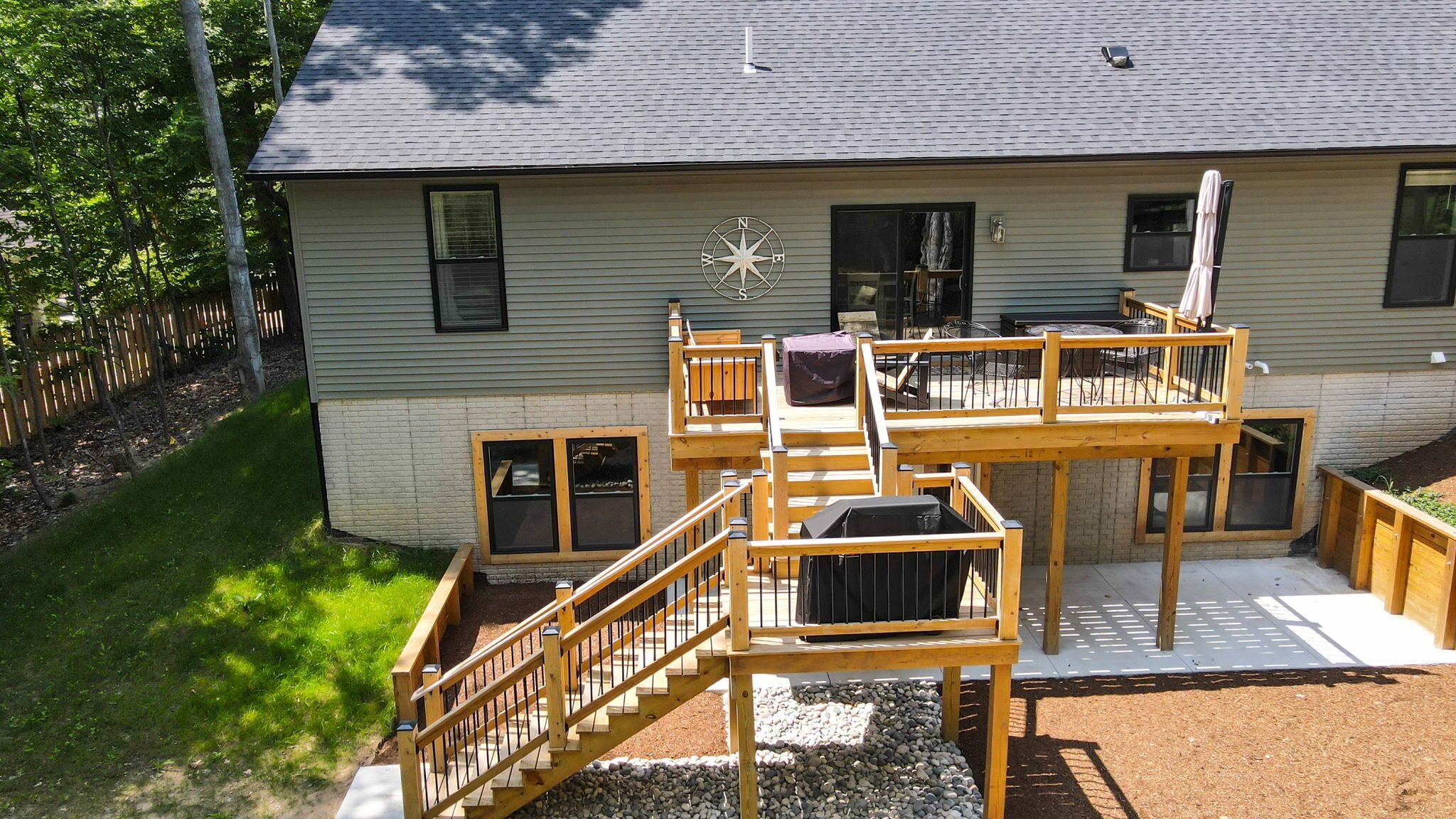 Une maison à deux étages avec une terrasse, un panneau indiquant les points cardinaux et un espace patio.